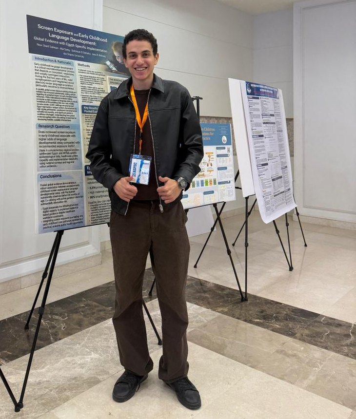 Alie Samy standing beside his research poster at a medical conference.